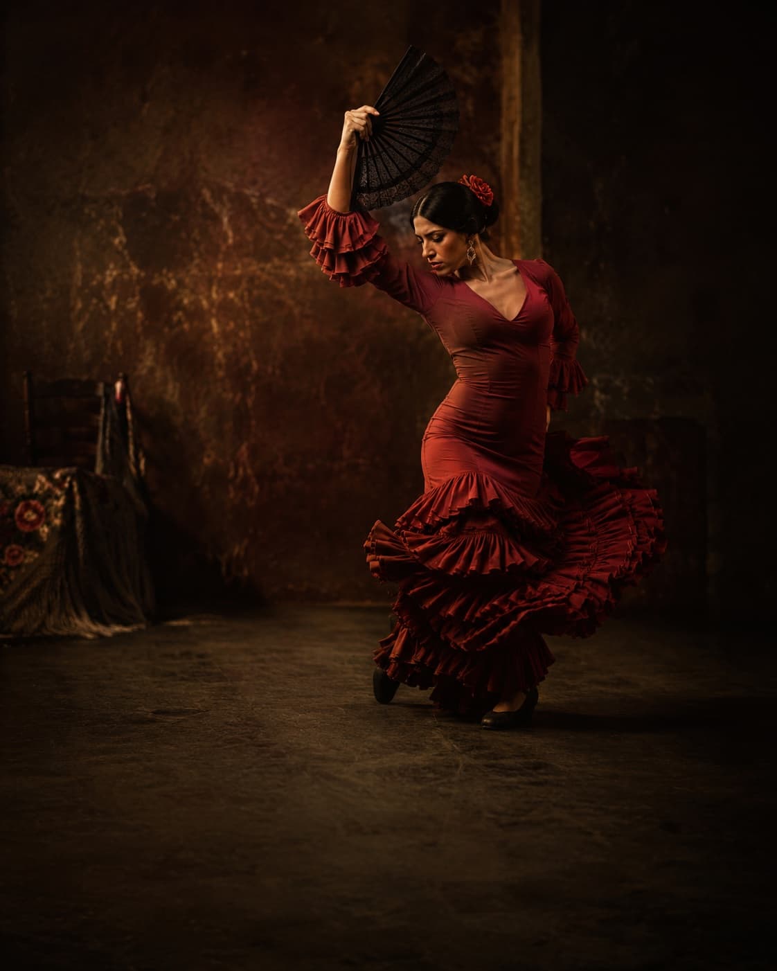 A flamenco dancer in a red dress holding a black lace fan aloft mid-performance